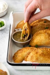 Photo of a hand dipping an Air Fryer Empanada in a small silver bowl with green salsa.
