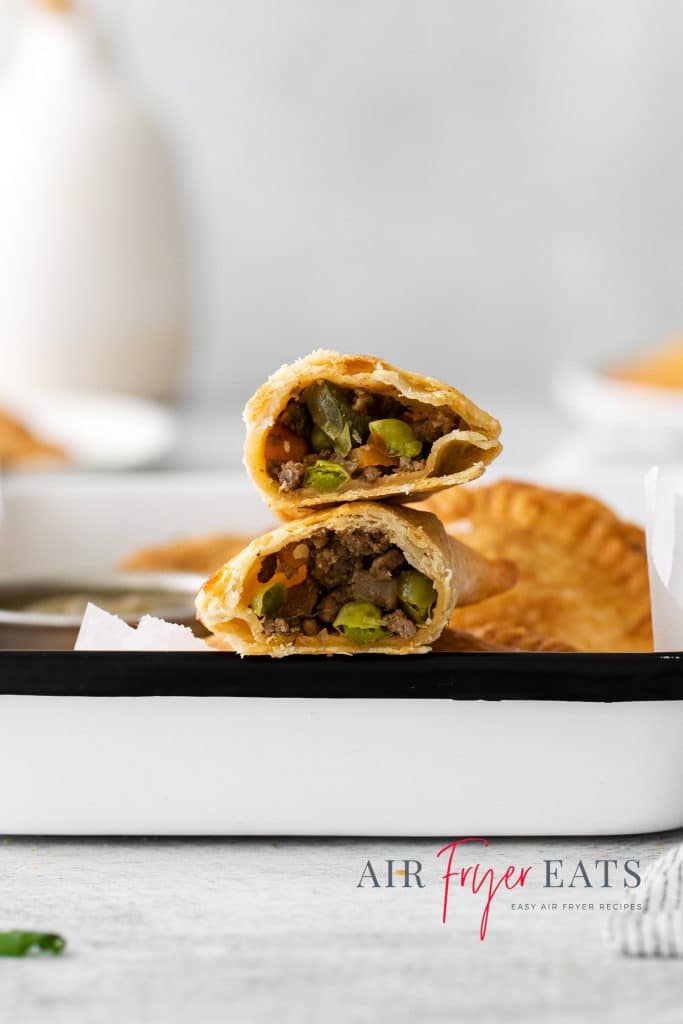 Photo of two air fryer empanadas, stacked on top of each other on a white platter, and cut open so you can see the inside filling.