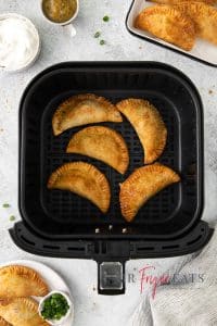 Top view photo of five empanadas in the air fryer basket, fully cooked, golden and crispy.