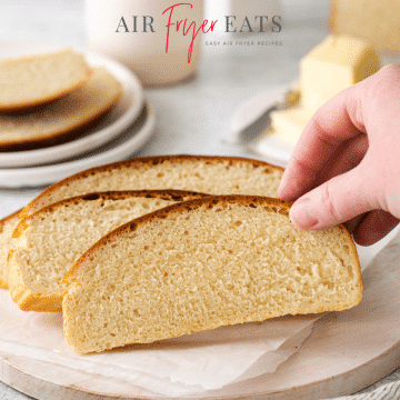 Photo of a hand grabbing a slice of Air Fryer Bread, which is on a wooden cutting board.