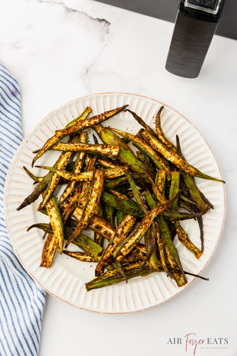 a plate of crispy air fryer sliced okra, next to an air fryer basket.