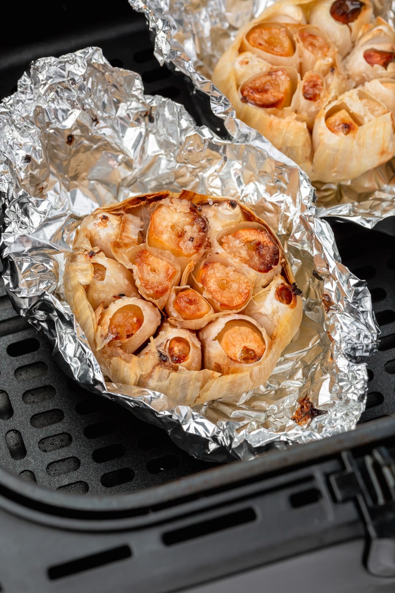 browned roasted whole garlic heads wrapped in foil, in an air fryer basket. 