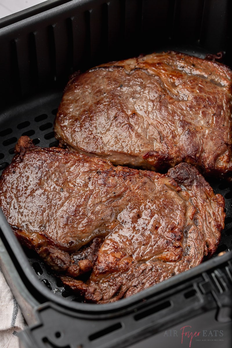 two leftover steaks reheating in a square cosori air fryer basket