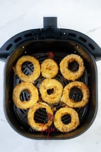 vertical photo showing 8 air fryer cheesy onion rings in an air fryer basket cooked