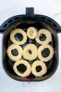 vertical photo showing 8 air fryer cheesy onion rings arranged in a single layer in an air fryer basket
