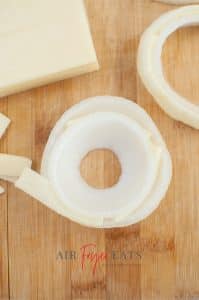 vertical photo showing sliced onion rings with slices of cheese between 2 rings on a wooden board