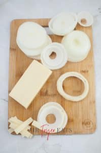 vertical photo showing sliced onion rings and cut cheese on a wooden board