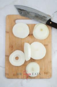 vertical photo showing sliced onion rings on a wooden board
