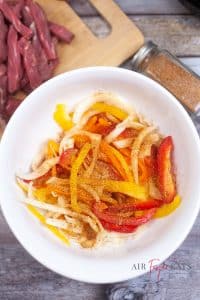 vertical photo of bell pepper and onion slices with fajita seasoning mixed in a bowl
