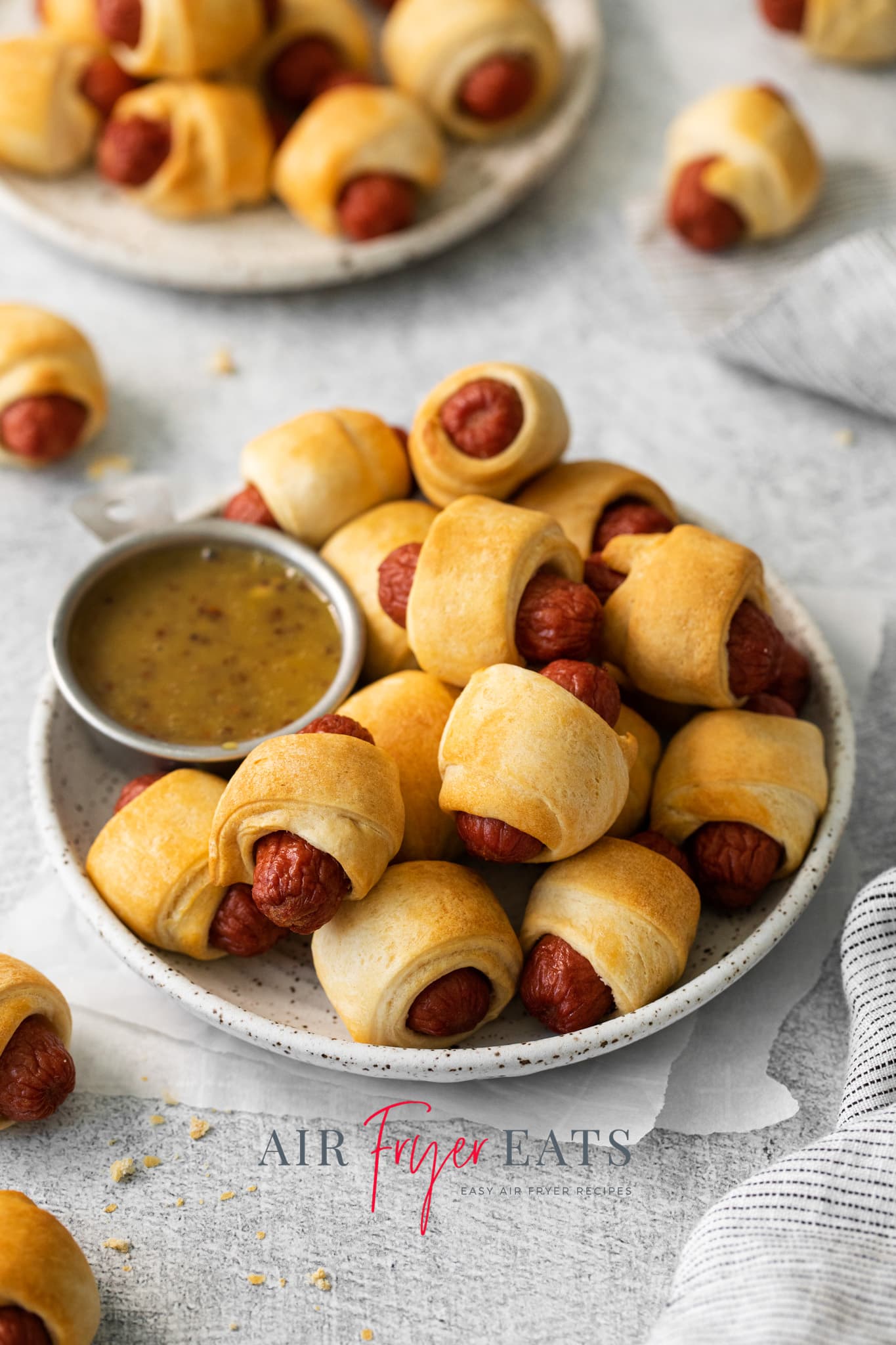Photo of a plate of Air Fryer Pigs in a Blanket, with a small silver dish filled with dipping sauce. 