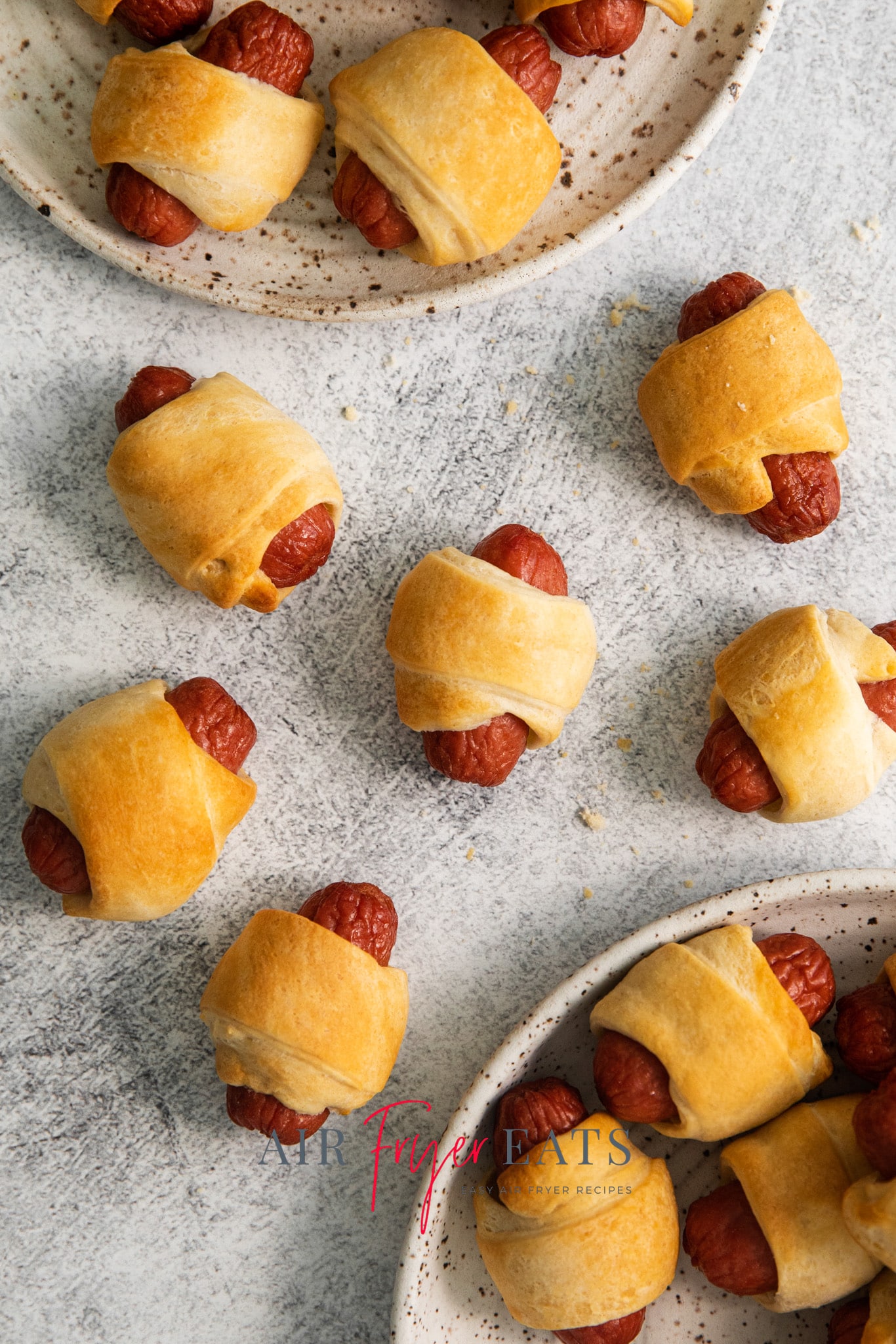 Top view photo of Pigs In A Blanket on plates and on the tabletop, ready to eat and golden brown. 