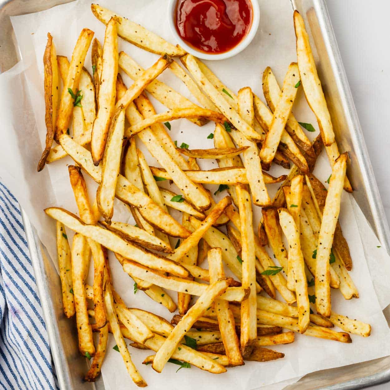 a small sheet pan lined with parchment paper, holding freshly cooked french fries and a small bowl of ketchup.