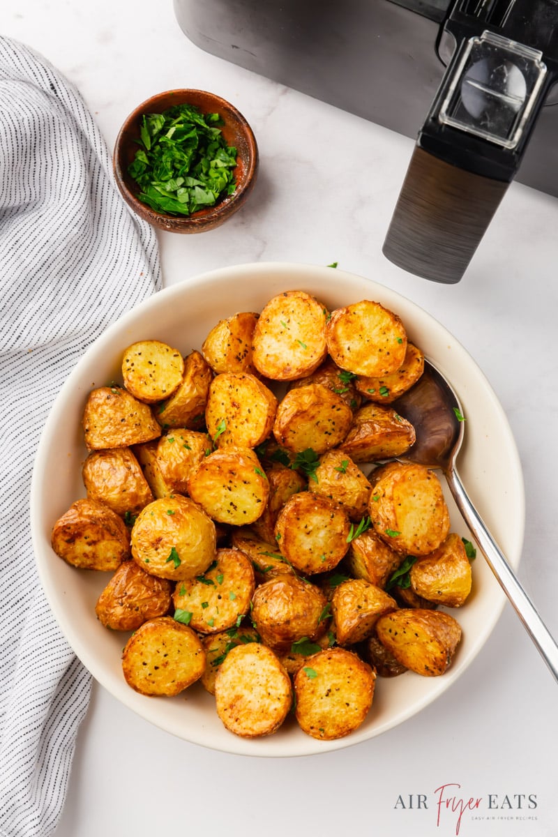 a white serving bowl filled with roasted potatoes next to a black air fryer basket. 