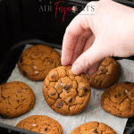 Photo of a hand grabbing a cookie from the air fryer basket that is golden brown and ready to enjoy.