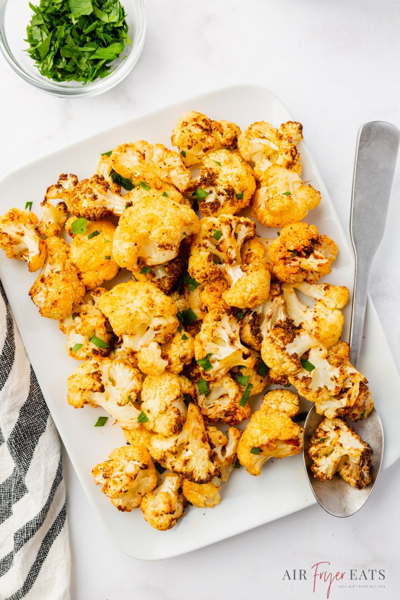 a rectangular platter of seasoned air fried cauliflower. A small cup of fresh parsley is above it. 