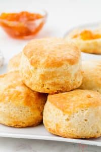 Photo of Air Fried Frozen Biscuits on a platter in a stack, with a glass bowl of apricot jam in the background.