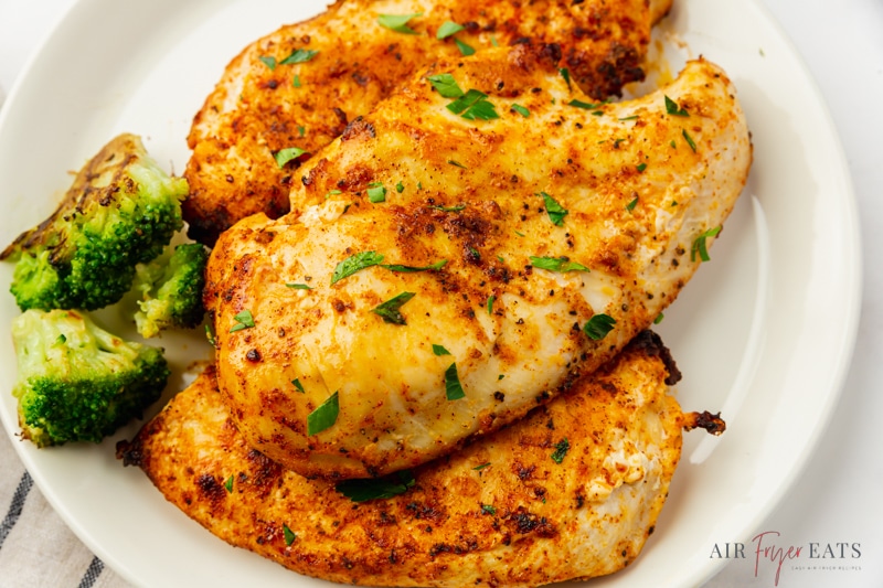 three cooked chicken breasts on a plate with a side of broccoli