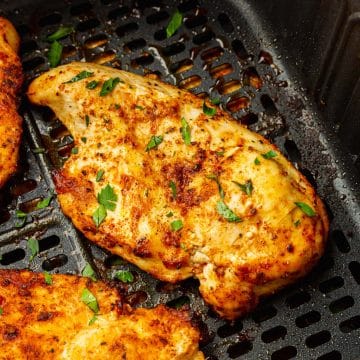 two cooked chicken breasts in a black square air fryer basket.