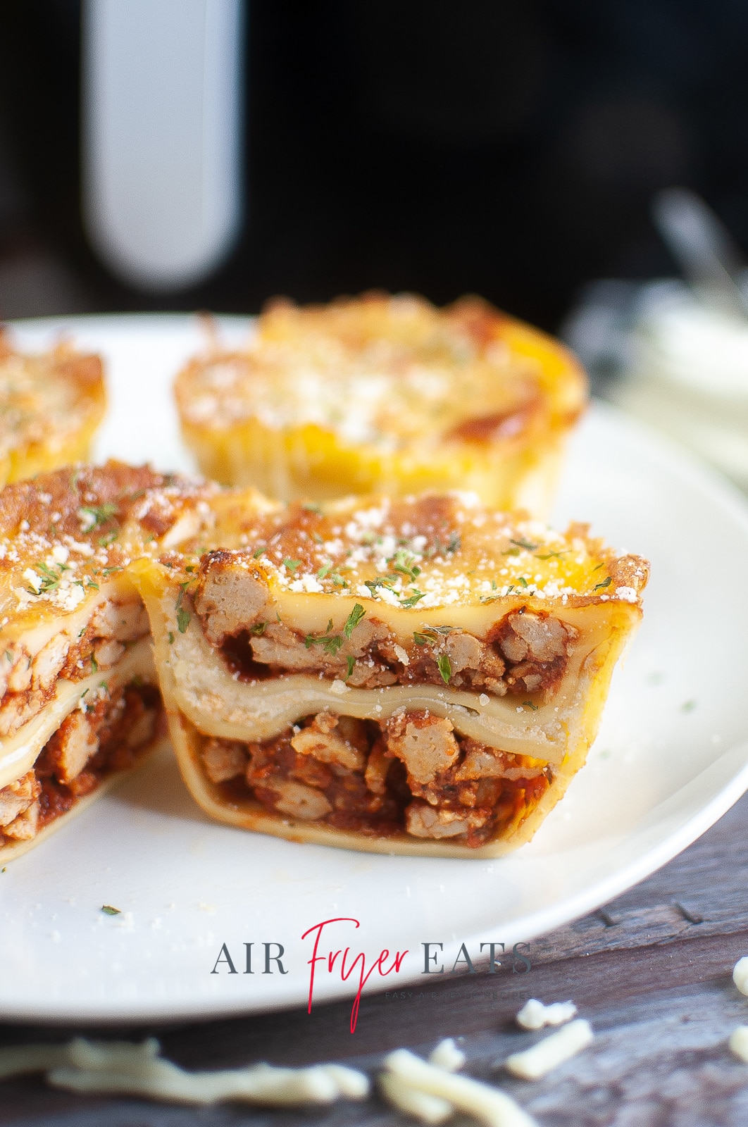 vertical photo showing air fryer lasagna cups with the one in the foreground cut in half to show the center. On a white plate