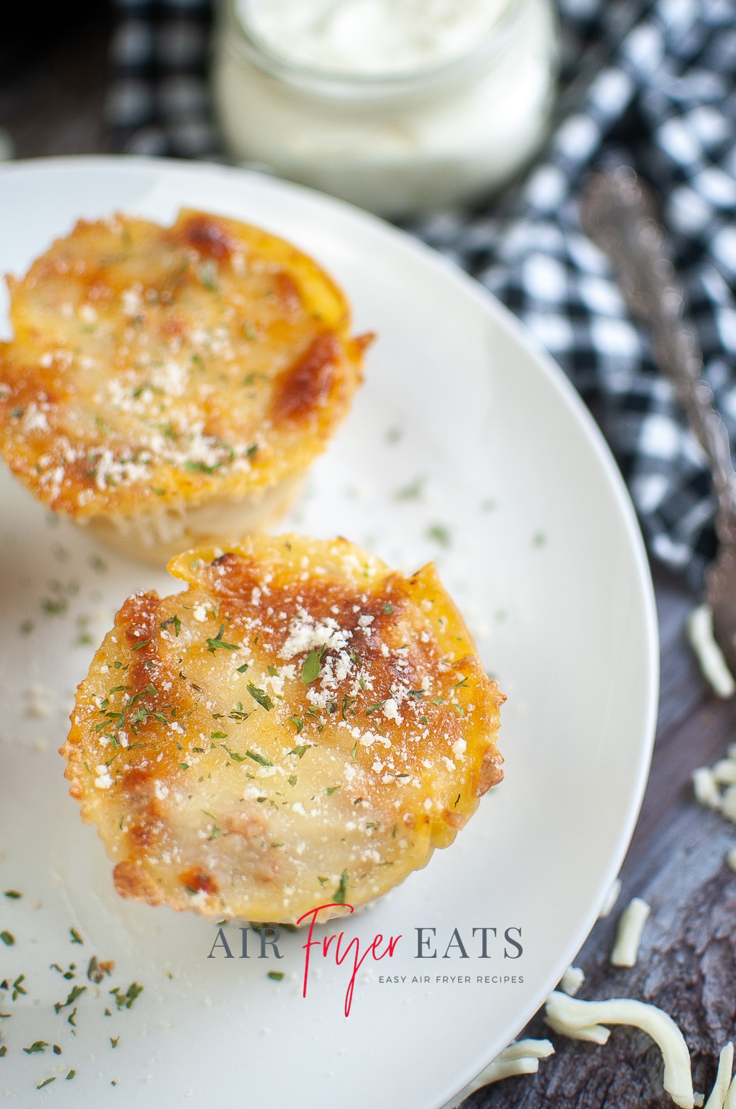 vertical photo showing 2 air fryer lasagna cups on a white plate, on a wooden surface