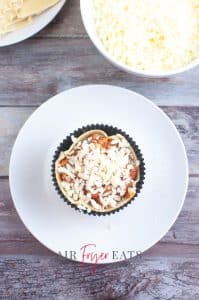 vertical photo showing cupcake mold with lasagna pasta lining and fully filled with layers and topped with mozzarella cheese