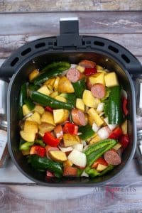 vertical photo showing all ingredients for air fryer sausage meal in the air fryer basket