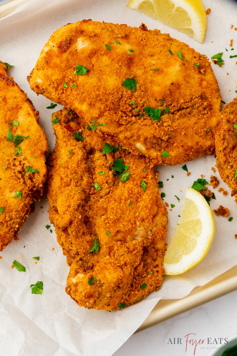 three pieces of fried chicken cutlets with lemon wedges. 
