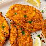 three pieces of fried chicken cutlets with lemon wedges.