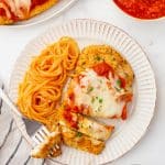 A white dinner plate with a piece of air fried chicken parmesan and a side of spaghetti.
