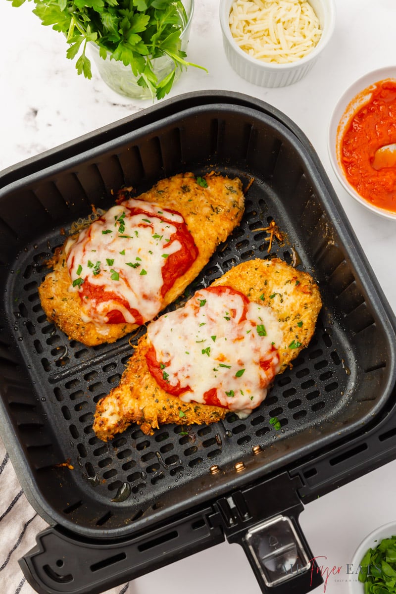 two pieces of chicken parmesan in a square air fryer basket.