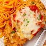 closeup image of air fryer chicken parmesan topped with sauce and cheese, with a side of spaghetti.