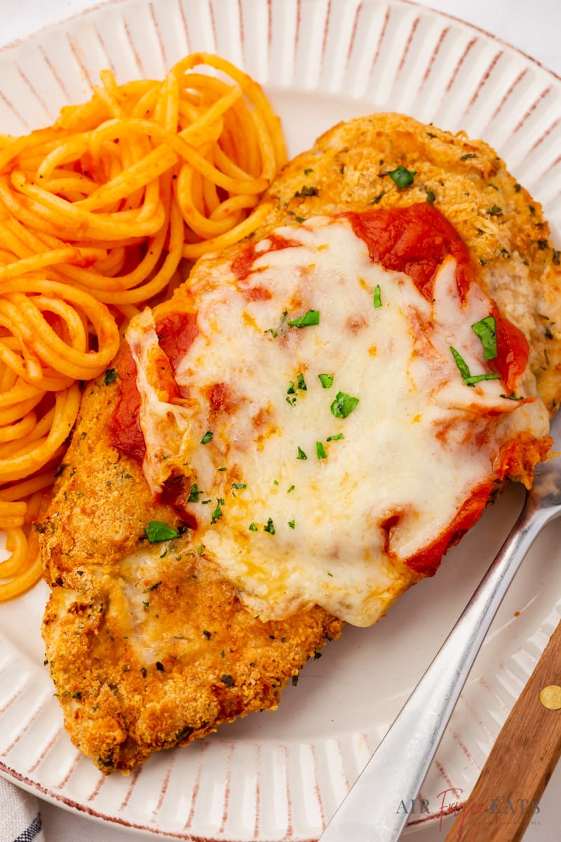 closeup image of air fryer chicken parmesan topped with sauce and cheese, with a side of spaghetti.