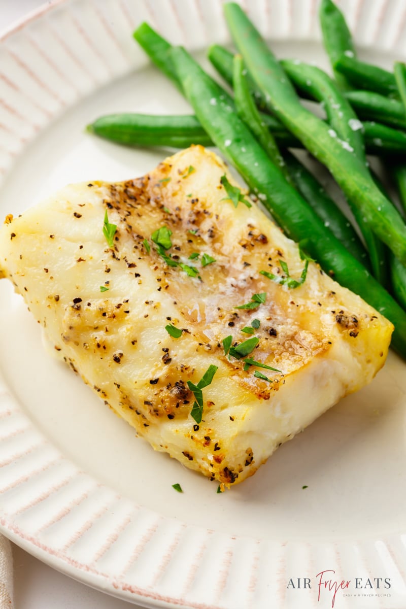 a piece of seasoned cod on a plate with green beans.