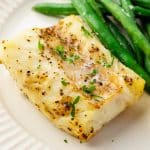 a piece of seasoned air fryer cod on a plate with green beans.