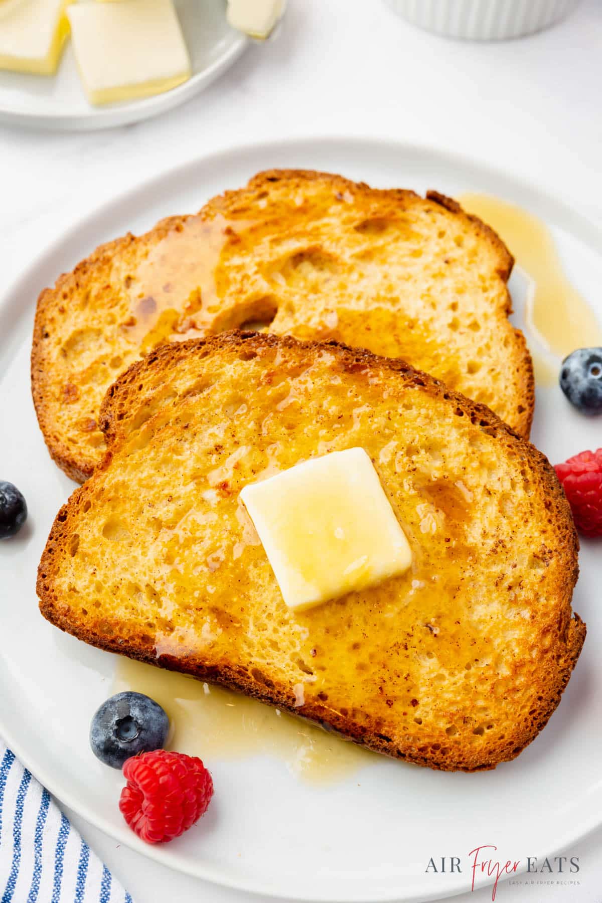 two slices of air fryer french toast on a plate topped with butter and syrup. 