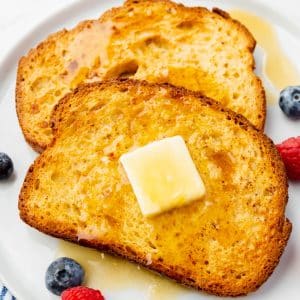 two slices of air fryer french toast on a plate topped with butter and syrup.