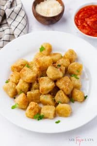 Photo of a white plate with a pile of crispy Air Fryer Cauliflower Gnocchi piled on top of eachother. There are two bowls of dipping sauces in the background.