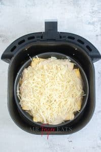 vertical photo showing cheese enchiladas in the air fryer basket, ready to be cooked