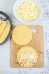 vertical photo showing tortillas, one with a little cheese, ready for rolling, a bowl of shredded cheese and a pan with rolled tortillas in
