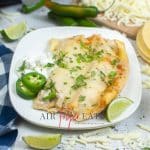 square photo showing a plate of air fryer cheese enchiladas with slices of green chiles, a lime wedge and a spoonful of sour cream