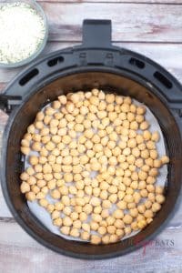 vertical photo of chickpeas in the parchment paper lined air fryer basket