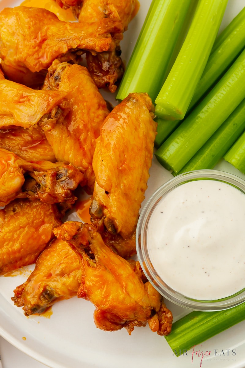 Closeup of a plate of air fryer buffalo wings with blue cheese and celery sticks. 