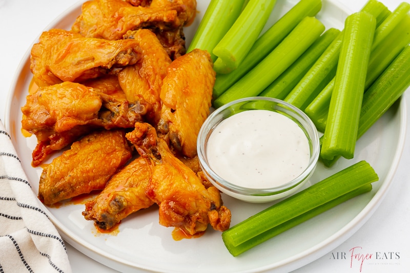 a plate of buffalo wings with celery and dip.