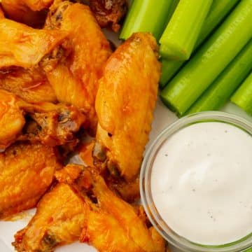 Closeup of a plate of air fryer buffalo wings with blue cheese and celery sticks.