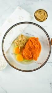 vertical photo showing a mixing bowl with peanut butter, pumpkin puree and eggs added