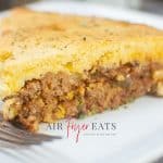 horizontal photo showing a slice of air fryer sloppy joe cornbread casserole on a square white plate with a fork also on the plate