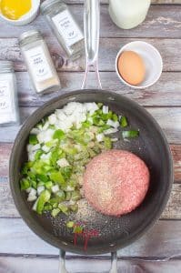 vertical photo showing ground beef, bell pepper and onion in a frying pan with other spices around the pan, all on a wooden surface