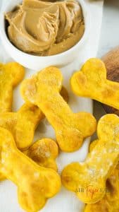 vertical photo showing air fryer dog treats with a bowl of peanut butter in the background