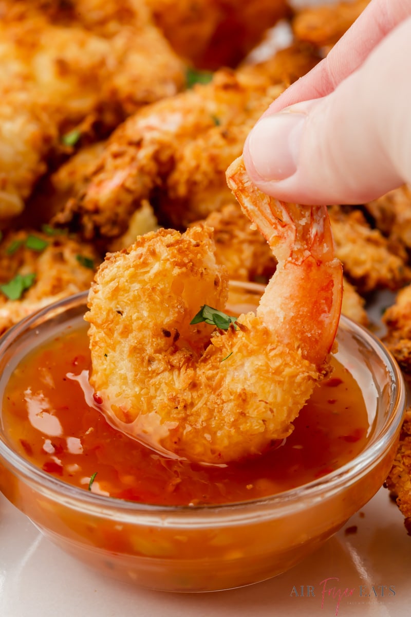 a coconut shrimp dipping into sweet chili sauce