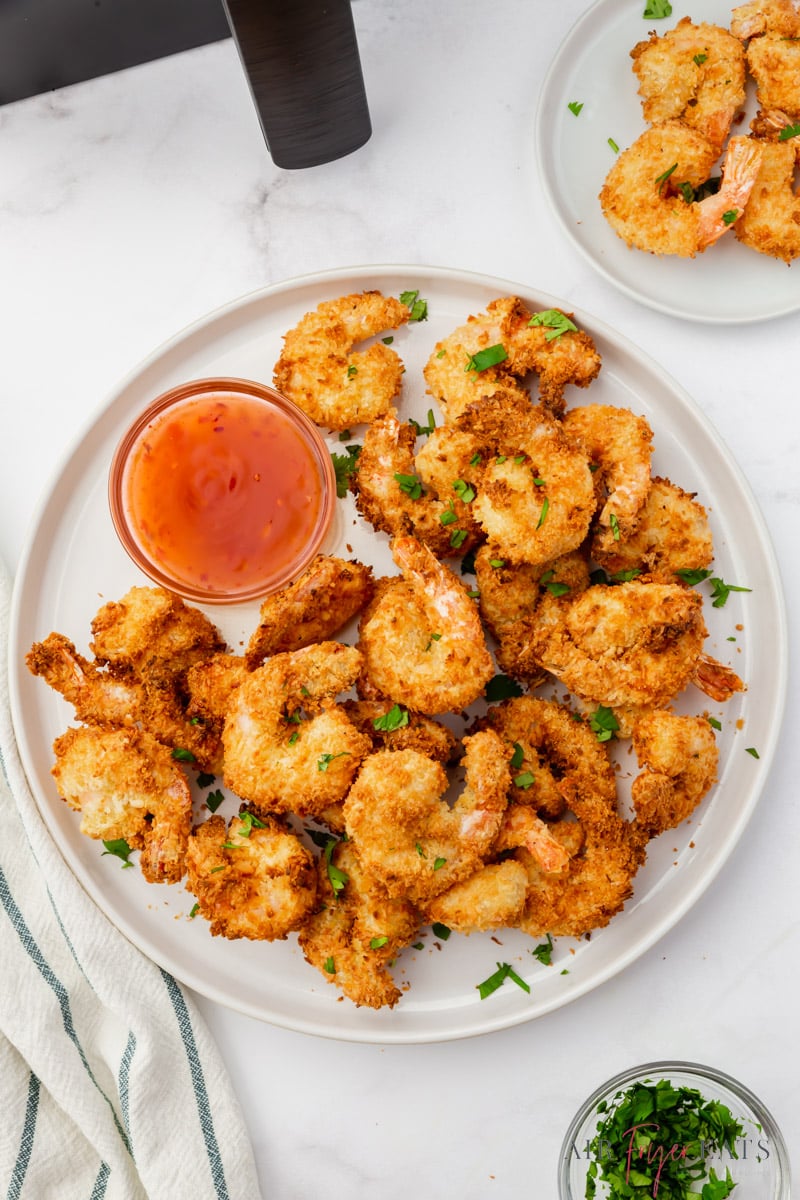 a plate of coconut shrimp with dipping sauce next to an air fryer.